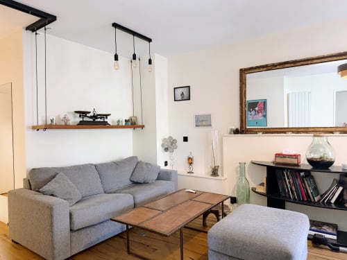 Salon moderne de l'appartement Maison ARLOÉ La Rochelle avec canapé gris, table basse en bois, étagères et luminaires suspendus