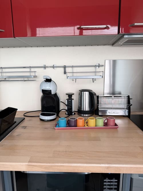 Comptoir de cuisine moderne à la Maison ARLOÉ avec cafetière, bouilloire, grille-pain et tasses colorées dans l'appartement de La Rochelle