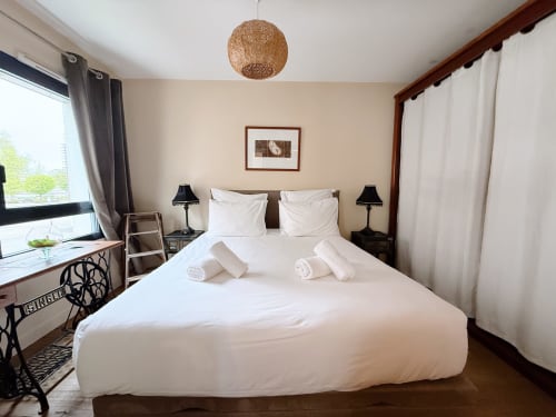 Chambre spacieuse à la Maison ARLOÉ à La Rochelle avec lit double, draps blancs, lampes de chevet noires et vue sur la ville