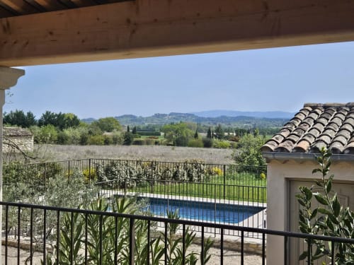 Poolside terrace overlooking Gordes countryside with stone buildings, cypress trees, and rolling hills in Provence