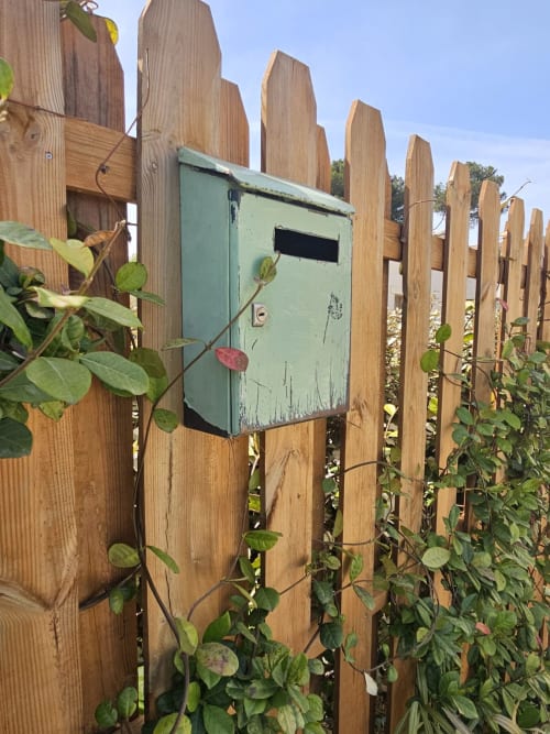 Weathered green mailbox on wooden fence with climbing ivy at Gordes property
