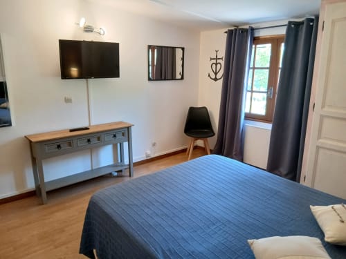 Chambre moderne du Mas d'Alivon à Arles avec literie bleue, télévision, bureau et portes donnant sur le jardin aux rideaux bleus