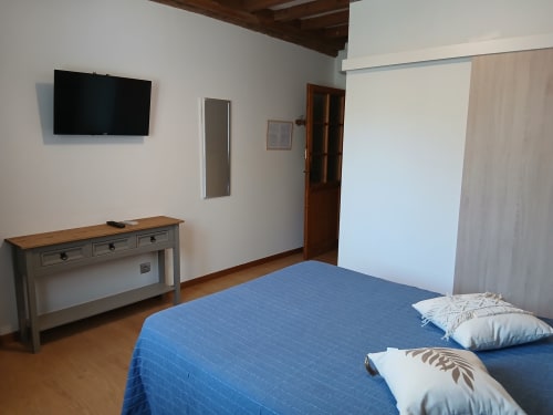 Chambre moderne du Mas d'Alivon à Arles avec literie bleue, téléviseur, bureau et poutres en bois