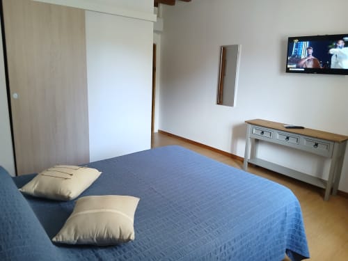 Chambre spacieuse du Mas D'Alivon à Arles avec lit bleu, oreillers crème, commode blanche, TV et parquet