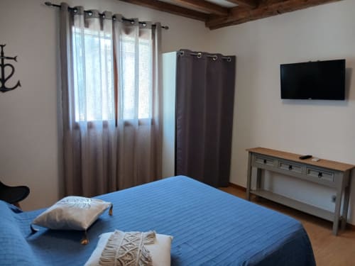 Chambre moderne au B&B Mas D Alivon à Arles avec lit bleu, télévision, bureau en bois et lumière naturelle des fenêtres voilées