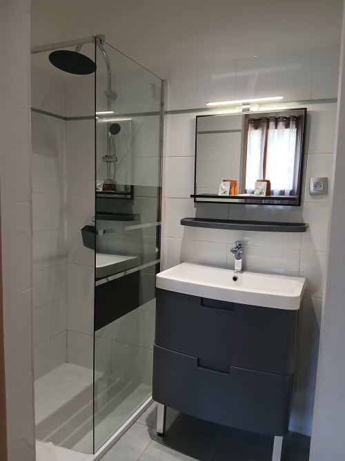 Salle de bain moderne au Mas D Alivon à Arles avec douche vitrée, vasque foncée, miroir et carrelage blanc