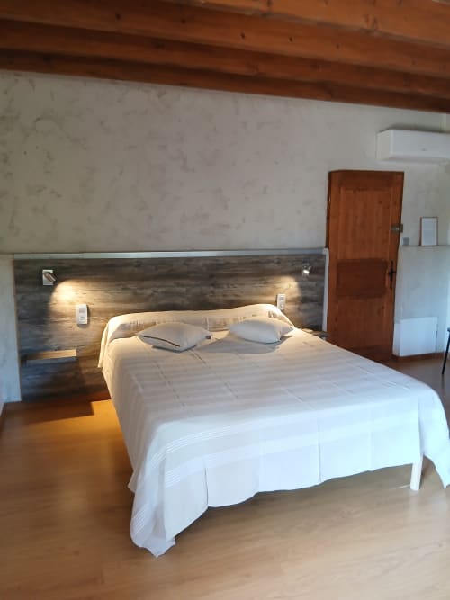 Chambre spacieuse du Mas d'Alivon avec literie blanche, tête de lit en bois éclairée et équipements modernes à Arles