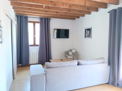 Chambre moderne au Mas d'Alivon à Arles avec canapé gris, poutres apparentes, TV et rideaux bleus