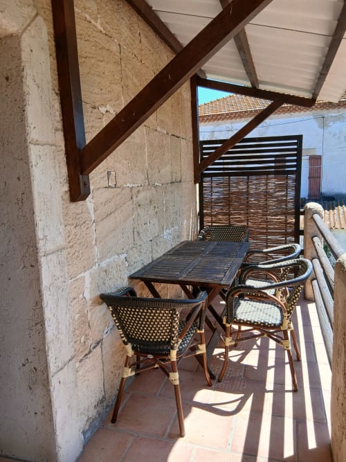 Balcon couvert du Mas d'Alivon à Arles : fauteuils en osier autour d'une table ombragée avec vue sur la campagne