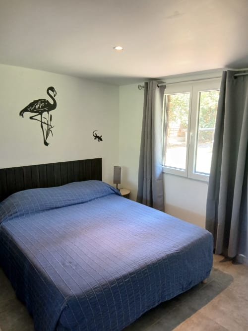 Chambre moderne au Mas d'Alivon Arles avec lit matelassé bleu, tête de lit noire, art mural flamant et portes-fenêtres