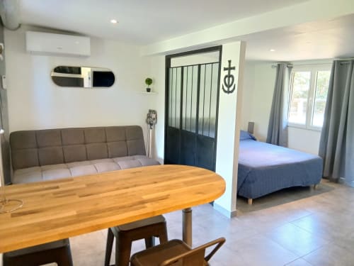 Chambre spacieuse et moderne au Mas d'Alivon à Arles avec table en bois, canapé-lit gris et chambre séparée