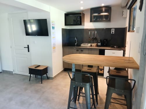 Cuisine du gîte Mas d'Alivon à Arles : comptoir en bois, crédence noire, télévision murale et électroménagers modernes