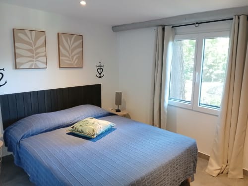 Chambre moderne au Mas D Alivon B&B à Arles avec literie bleue, tête de lit noire et portes vitrées ouvertes sur le jardin
