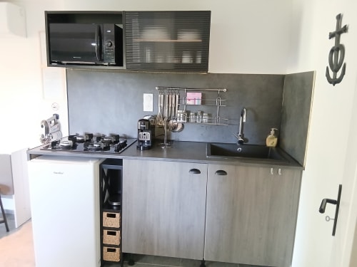 Kitchenette moderne au Mas d'Alivon à Arles avec cuisinière à gaz, évier, crédence foncée et micro-ondes mural.