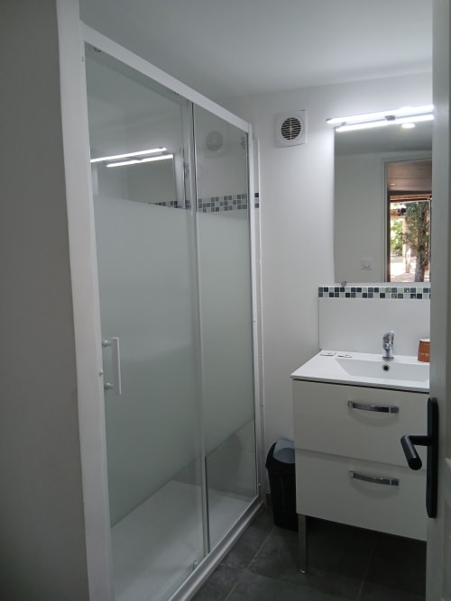 Salle de bains moderne au Mas D Alivon à Arles avec douche vitrée, meuble-lavabo blanc et finitions carrelées