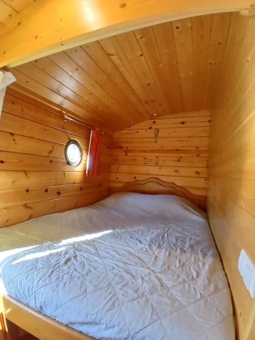 Chambre chaleureuse en bois à la Roulotte du Mas d'Alivon à Arles, avec lit et hublot