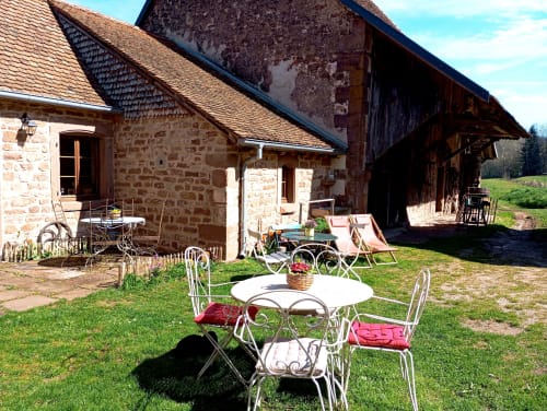 Jardin de la pension Paulusmühle avec table et chaises de bistrot en métal, bâtiment en pierre rustique à toiture d'ardoise à Soucht, France
