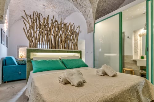 Camera moderna a Pietra & Luce a Ostuni con testata verde, biancheria color crema, arte in legno galleggiante e poltrona teal