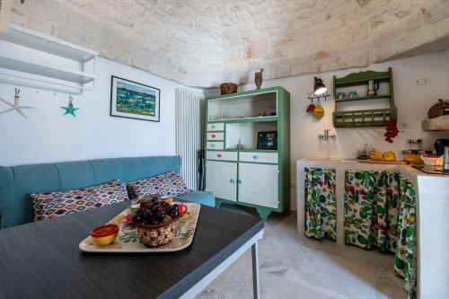 Appartamento stile Ostuni a Pietra & Luce con divano turchese, mobile contenitore verde e angolo cottura attrezzato