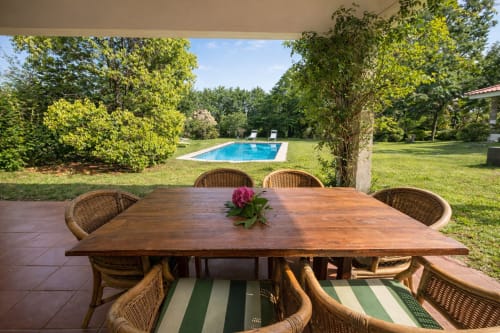 Terraza cubierta con mesa de comedor con vistas a la piscina y jardines de la villa Holibai enfrente del rio Miño. Galicia