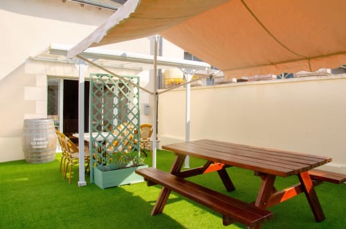 Terrasse extérieure des Relais-Orbigny avec tables de pique-nique, gazon synthétique vert, voile d'ombrage orange et zone de détente