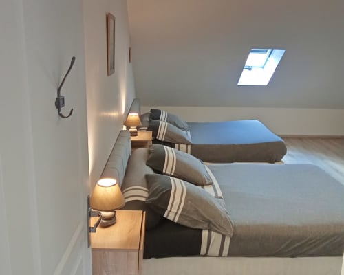 Chambre cosy mansardée aux Relais-Orbigny avec lits jumeaux, coussins rayés, lucarne et lampes de chevet à Orbigny