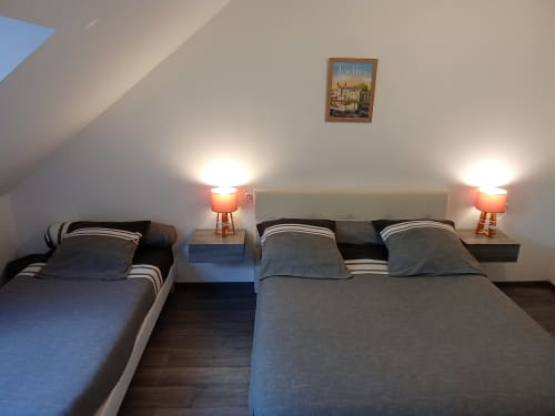 Chambre douillette aux Relais-Orbigny avec deux lits, tête de lit beige, lampes de chevet et affiche des Lochs.