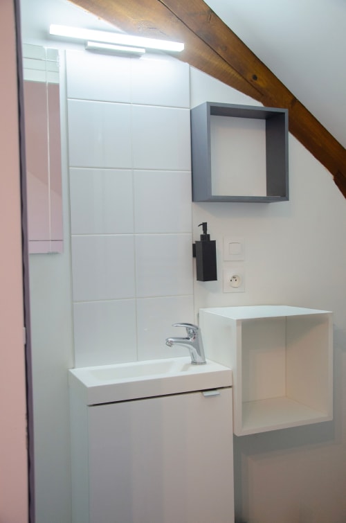 Salle de bain moderne aux Relais-Orbigny avec lavabo blanc, miroir gris et douche carrelée