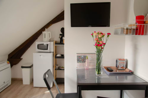 Kitchenette du studio avec table de salle à manger, œillets roses, téléviseur écran plat et escalier en bois aux Relais-Orbigny
