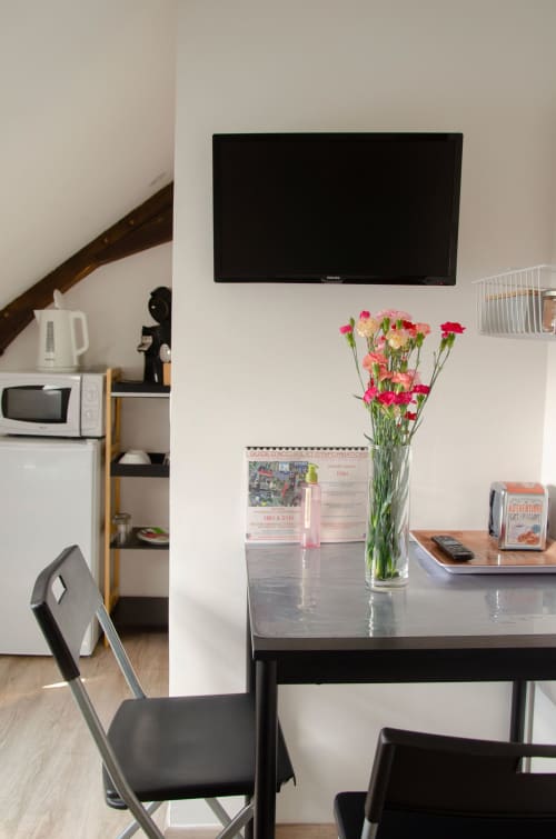 Chambre moderne aux Relais-Orbigny avec table à manger, œillets roses, TV murale et mobilier contemporain