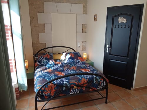 Chambre lumineuse aux Relais-Orbigny avec linge de lit coloré à motifs, lit en métal noir et vue sur le jardin
