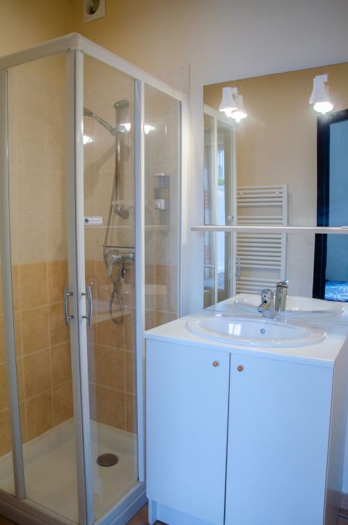 Salle de bains moderne aux Relais-Orbigny avec double vasque, cabine de douche en verre et meuble-lavabo blanc au Relais du