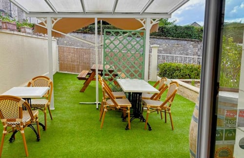 Terrasse extérieure des Relais-Orbigny avec gazon synthétique vert, tables de restauration, chaises en rotin et pergola ombragée à Orbigny,