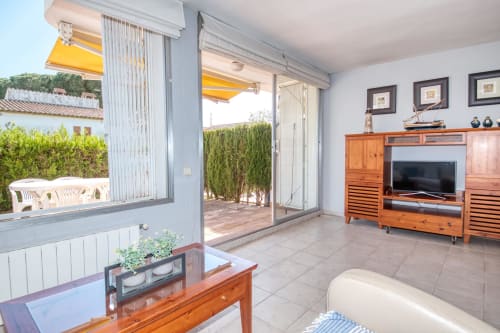 Saló lluminós a Finques Garcia Enrich de Palafrugell amb aonament groc, vista a terrassa, mobles de fusta i pantalla plana