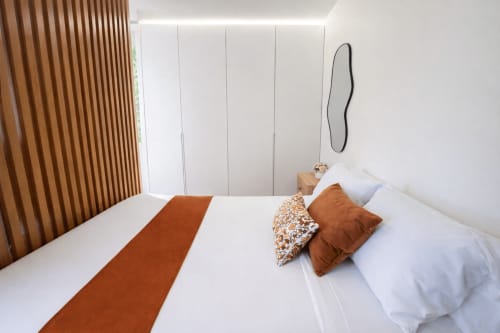 Dormitorio moderno en Holibai de Baiona con ropa de cama blanca, detalles en terracota y elementos de madera