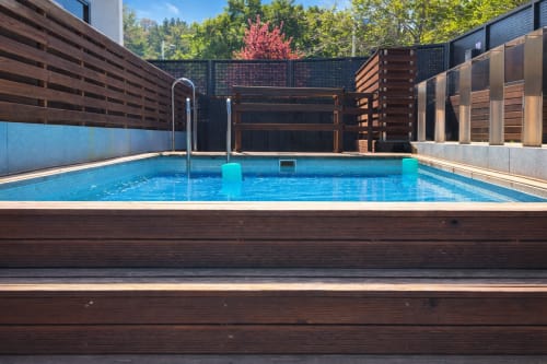 Piscina moderna con terraza de madera en Holibai, Baiona, rodeada de vistas a la montaña y privacidad de madera