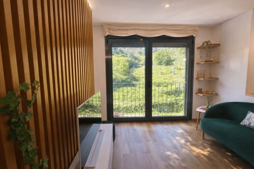 Sala de estar moderna con vistas a las montañas, pared de listones de madera, sofá verde y puertas de cristal hacia colinas exuberantes