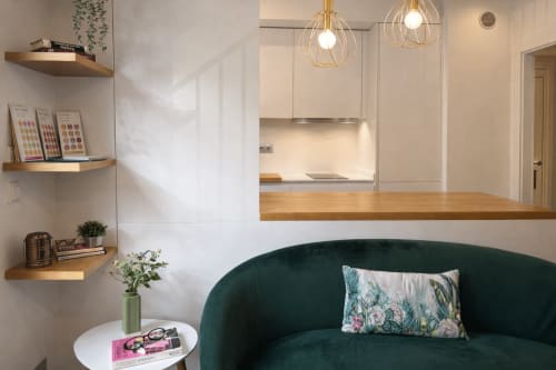 Salón moderno de apartamento en Baiona con sofá verde oscuro, encimera de madera, lámparas colgantes doradas y estanterías blancas