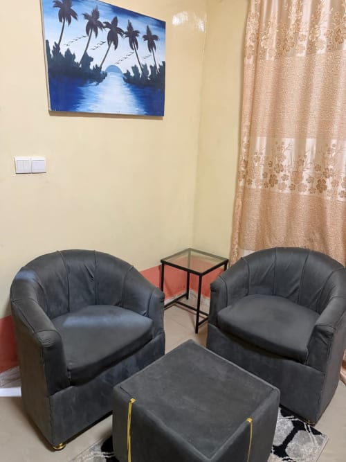 Espace lounge moderne de la chambre Bandia à l'hôtel Keur Medzo, Lac Rose, avec fauteuils en cuir noir et œuvres d'art tropical