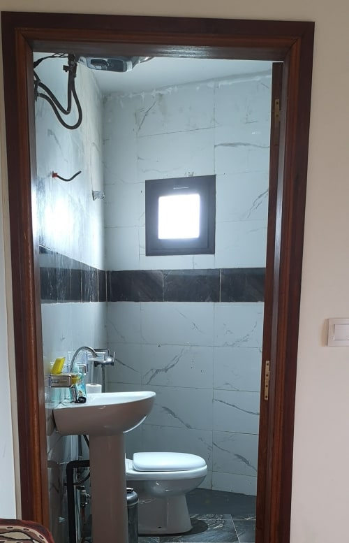 Salle de bains moderne avec carrelage en marbre, lavabo sur colonne, toilettes et éclairage encastré à l'hôtel Keur Medzo, Lac Rose
