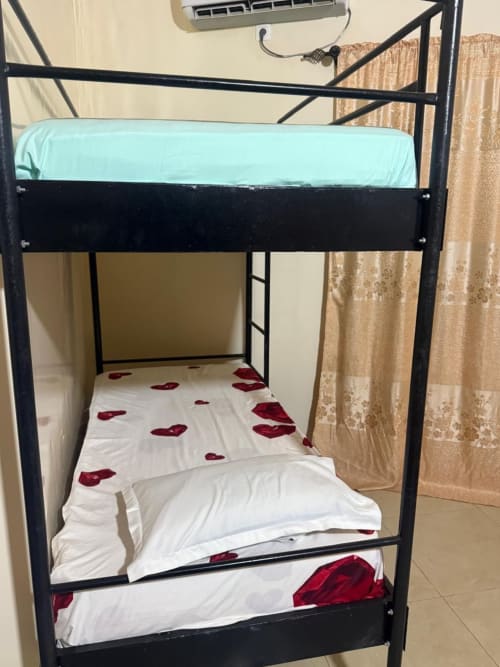 Lit à baldaquin en métal noir avec drap housse bleu clair et literie blanche parsemée de pétales de roses rouges à l'hôtel Keur Medzo Lac Rose