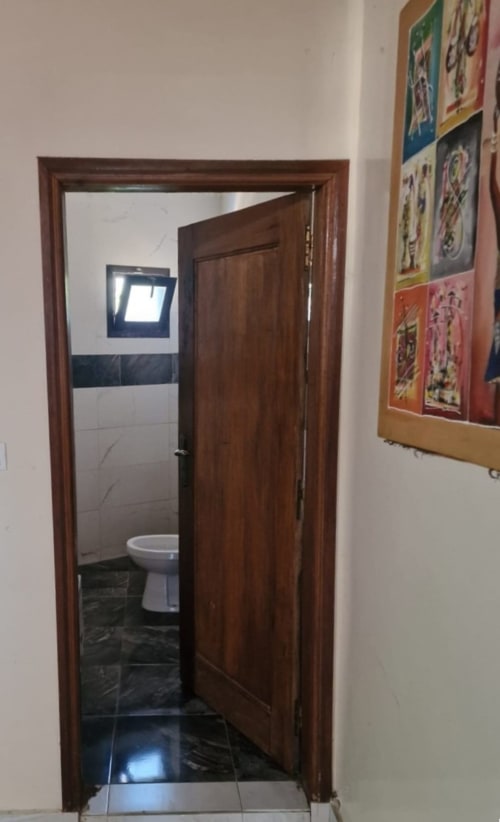 Porte en bois ouverte montrant la salle de bain avec toilettes de l'hôtel Keur Medzo Lac Rose à Niaga