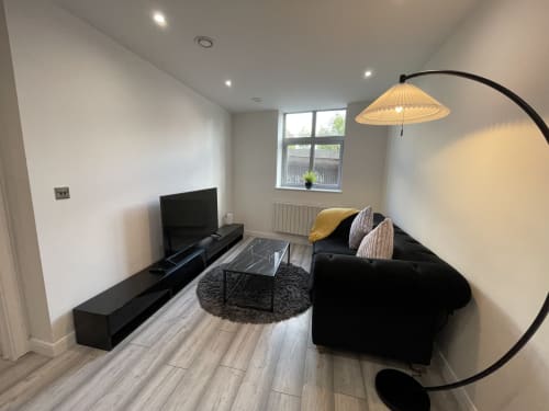 Modern living room in Leicester serviced apartment with black sofa, TV, arched lamp, and city views