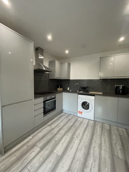 Modern kitchen in Empire Serviced Apartments Leicester with white cabinetry, black countertops, built-in oven, washing