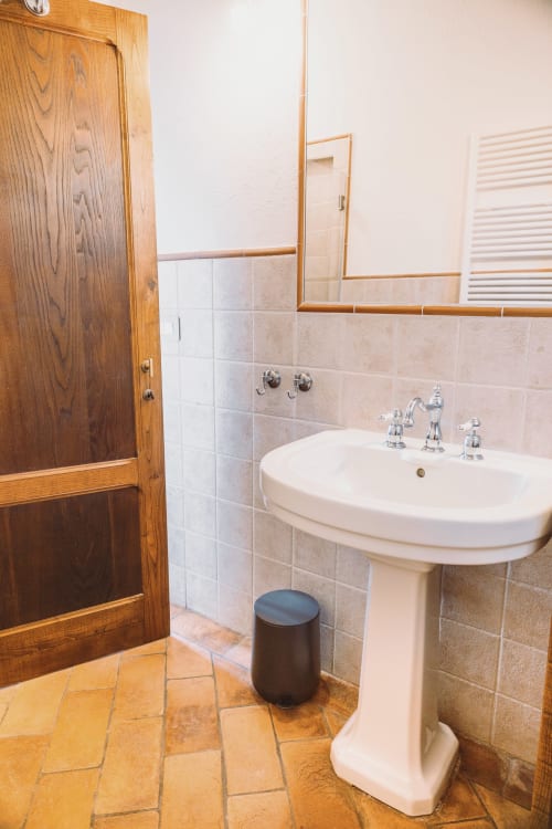 Bagno privato con lavabo a colonna e porta in legno nella camera La Vigna dell'Agriturismo Il Serraglio, Montepulciano