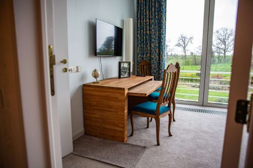 Chambre d'hôtel à Villa Bianca avec bureau en bois, chaise bleue, télévision et vue sur le jardin par grandes fenêtres à Mortroux Dalhem
