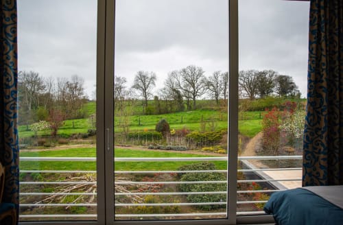 Vue sur le jardin depuis la chambre de Villa Bianca à Mortroux Dalhem, Belgique - paysage pastoral avec champs verts et arbres dénudés