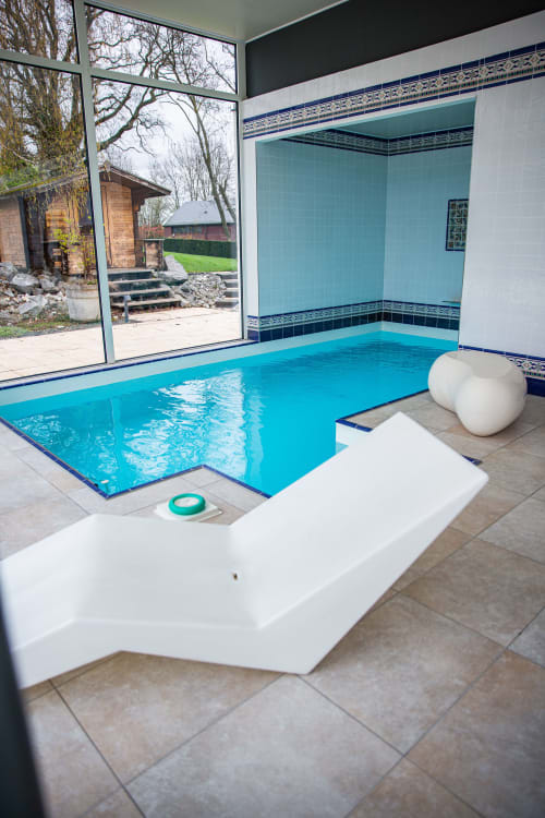 Piscine intérieure moderne aux eaux turquoise à Villa Bianca, Belgique, avec chaises longues blanches et vue sur le jardin.
