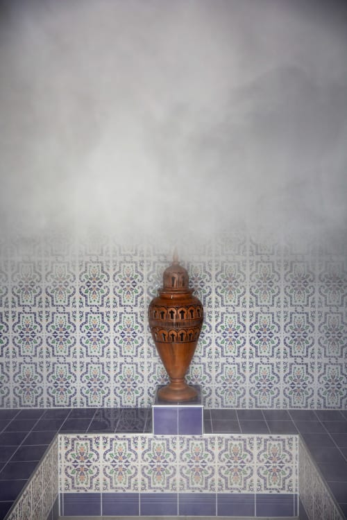Urne en cuivre ornementée sur piédestal devant un mur de carreaux à motifs décoratifs dans la chambre de la Villa Bianca