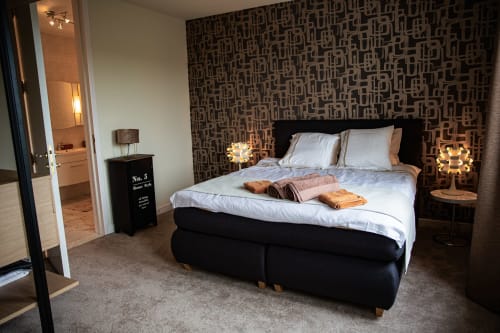 Chambre double moderne à la Villa Bianca B&B à Dalhem avec lit noir, mur d'accent à motifs, draps blancs et salle de bain privée